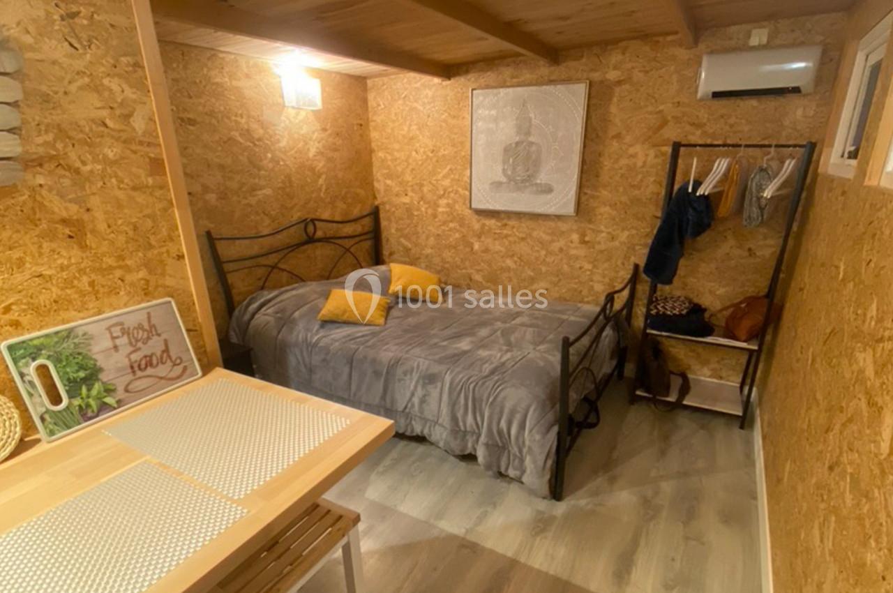 Chambre avec lit double, murs en bois, table avec chaises, portant avec vêtements et éclairage chaleureux.