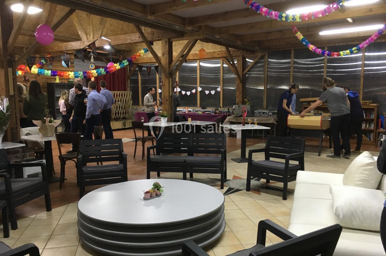 Salle décorée pour un événement avec des guirlandes colorées, des tables empilées et des personnes discutant ou jouant.