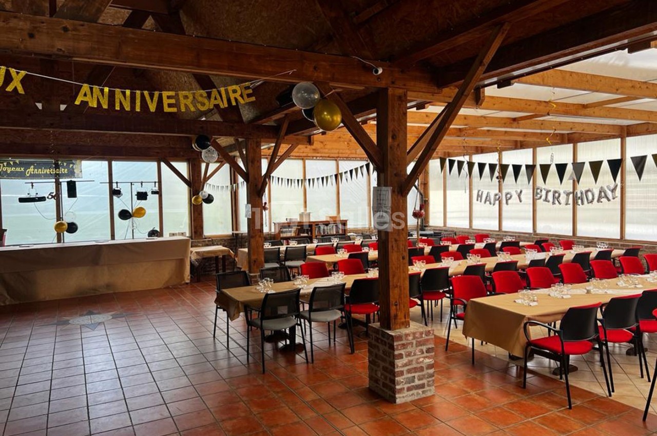 Salle décorée pour un anniversaire avec tables alignées, chaises rouges et guirlandes suspendues dans un espace lumineux.