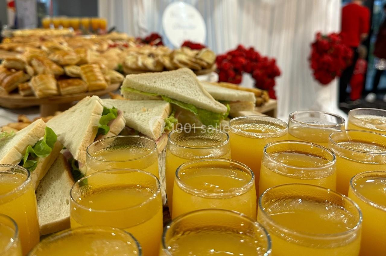 Plateau de sandwichs et viennoiseries accompagné de verres de jus d'orange sur une table de buffet.