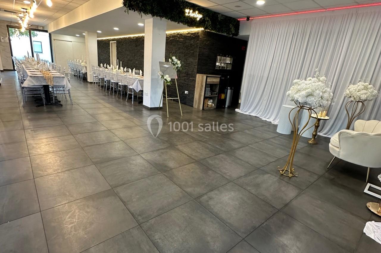 Salle de réception moderne avec tables dressées, sol en carrelage gris, éclairage suspendu et décor floral.