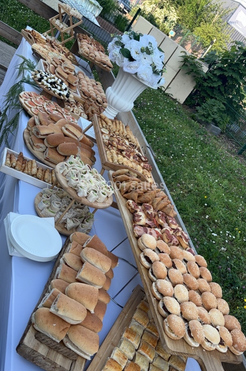 Buffet en extérieur avec une variété de sandwichs, amuse-bouches et pâtisseries disposés sur des tables blanches.