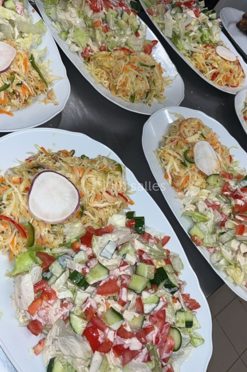 Assiettes de salades variées avec légumes frais, fromage râpé et sauce, disposées sur une table en inox.