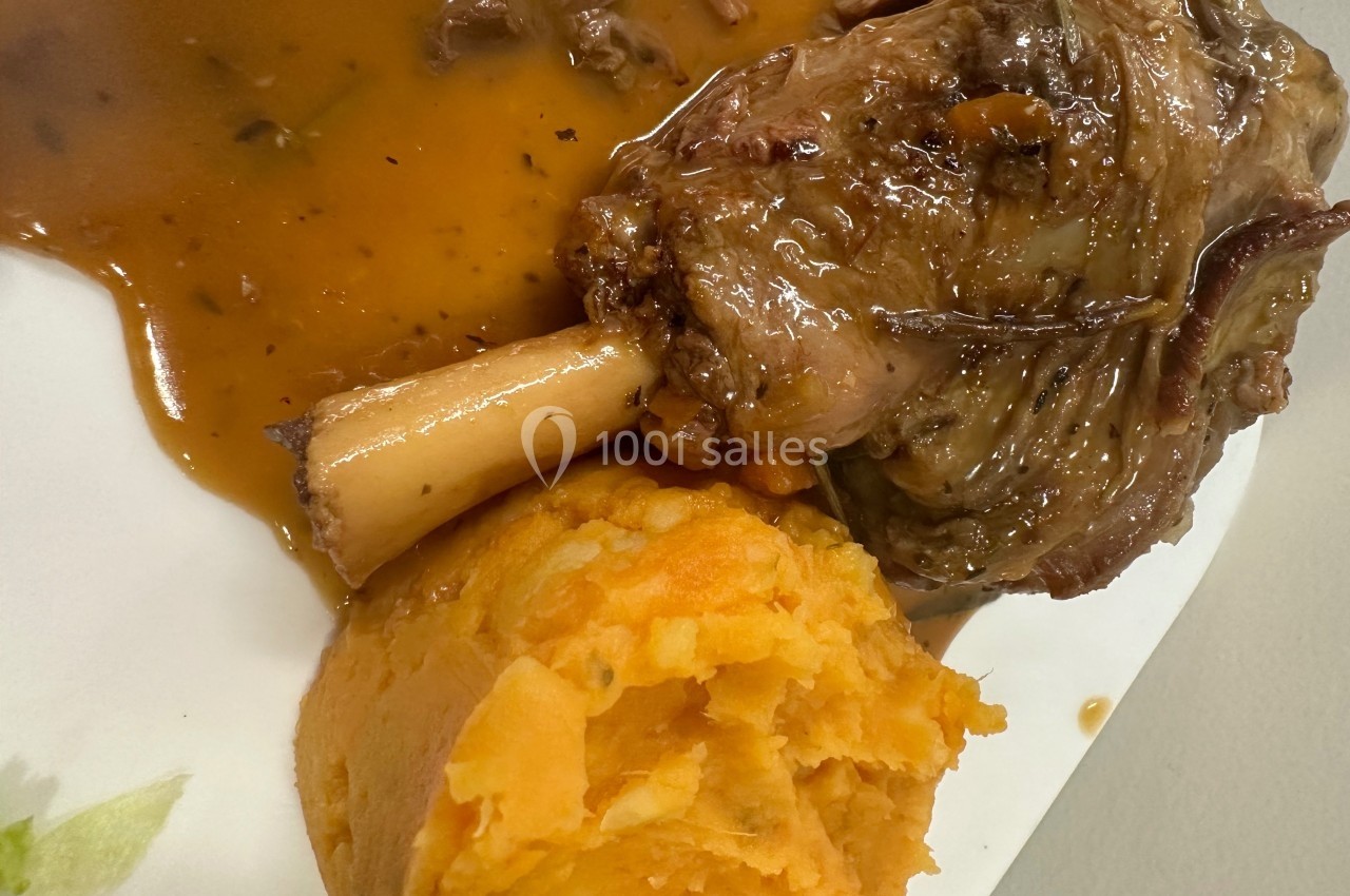 Plat composé d'un jarret d'agneau braisé avec sauce, accompagné de purée de patates douces sur une assiette blanche.