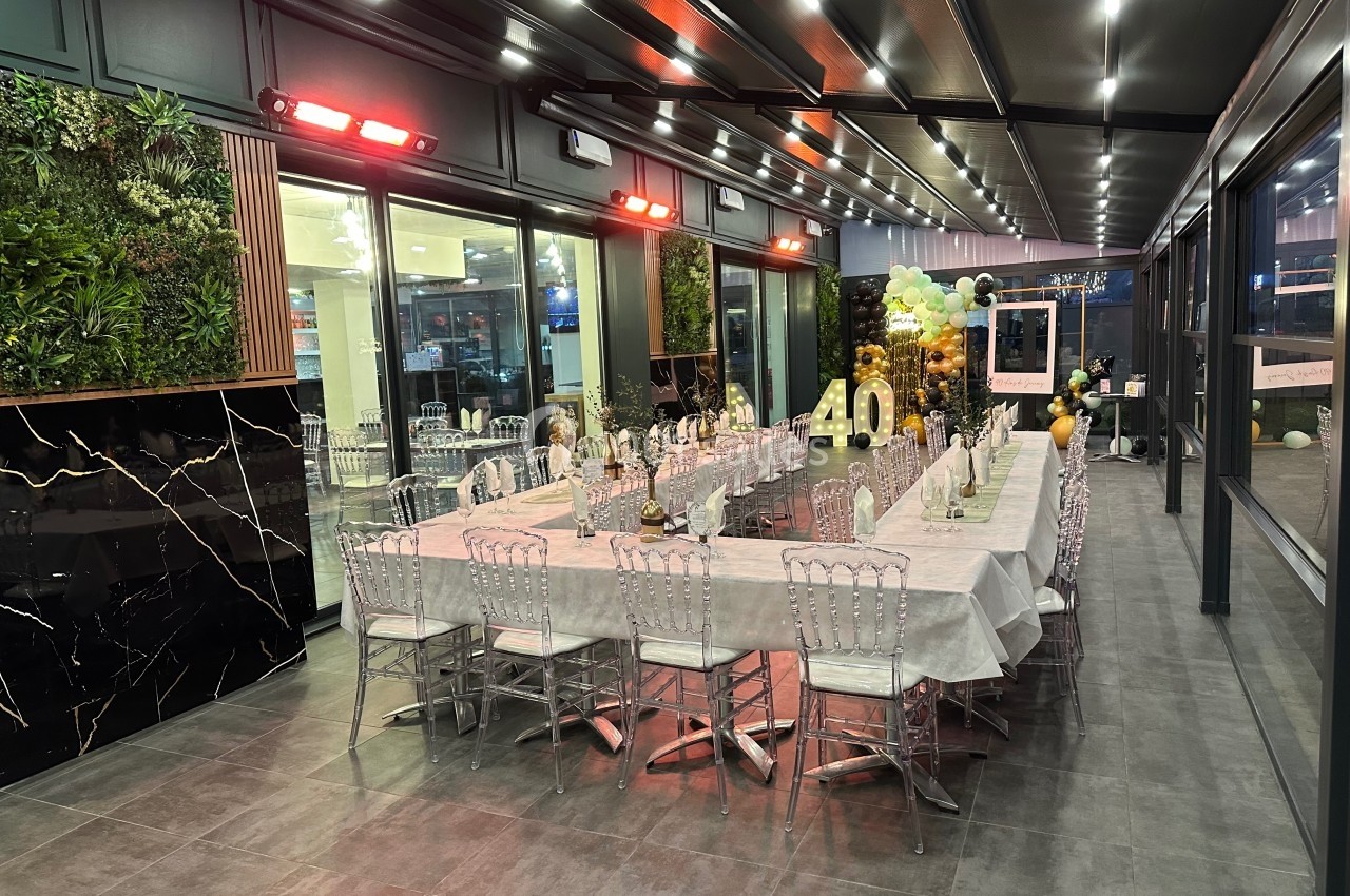 Salle décorée pour une réception avec une grande table dressée, des chaises transparentes et des ballons en arrière-plan.