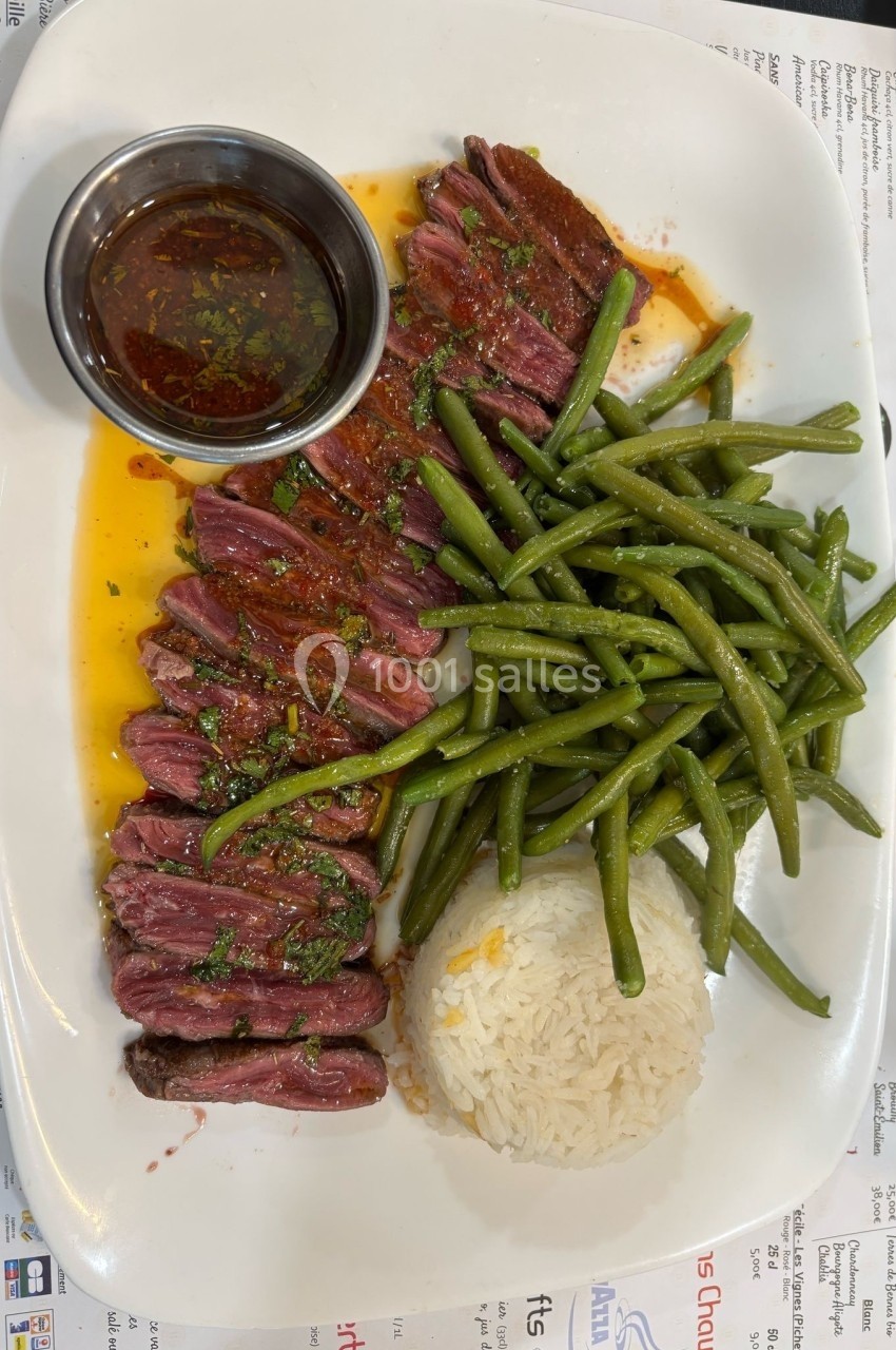 Assiette composée de tranches de viande saignante, haricots verts, riz blanc et sauce servie dans un ramequin.