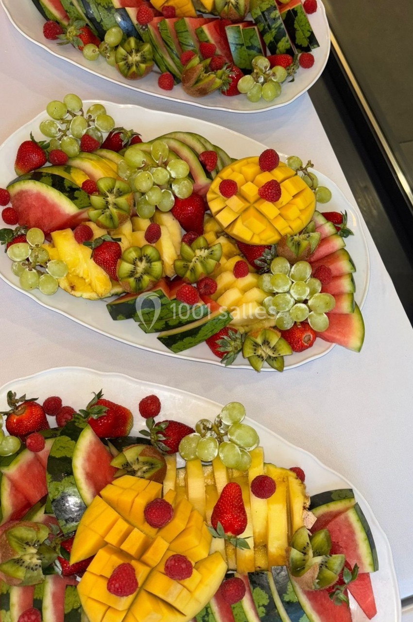 Plateaux de fruits frais composés de mangues, pastèques, fraises, raisins et kiwis, disposés sur une nappe blanche.
