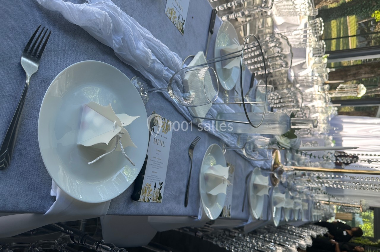 Table dressée élégamment avec nappes grises, assiettes blanches, menus imprimés et verres disposés pour un événement.