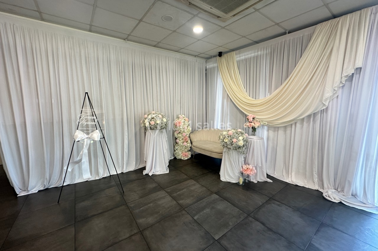 Décor intérieur avec rideaux blancs, fauteuil beige, fleurs pastel et éclairage doux dans une salle carrelée.
