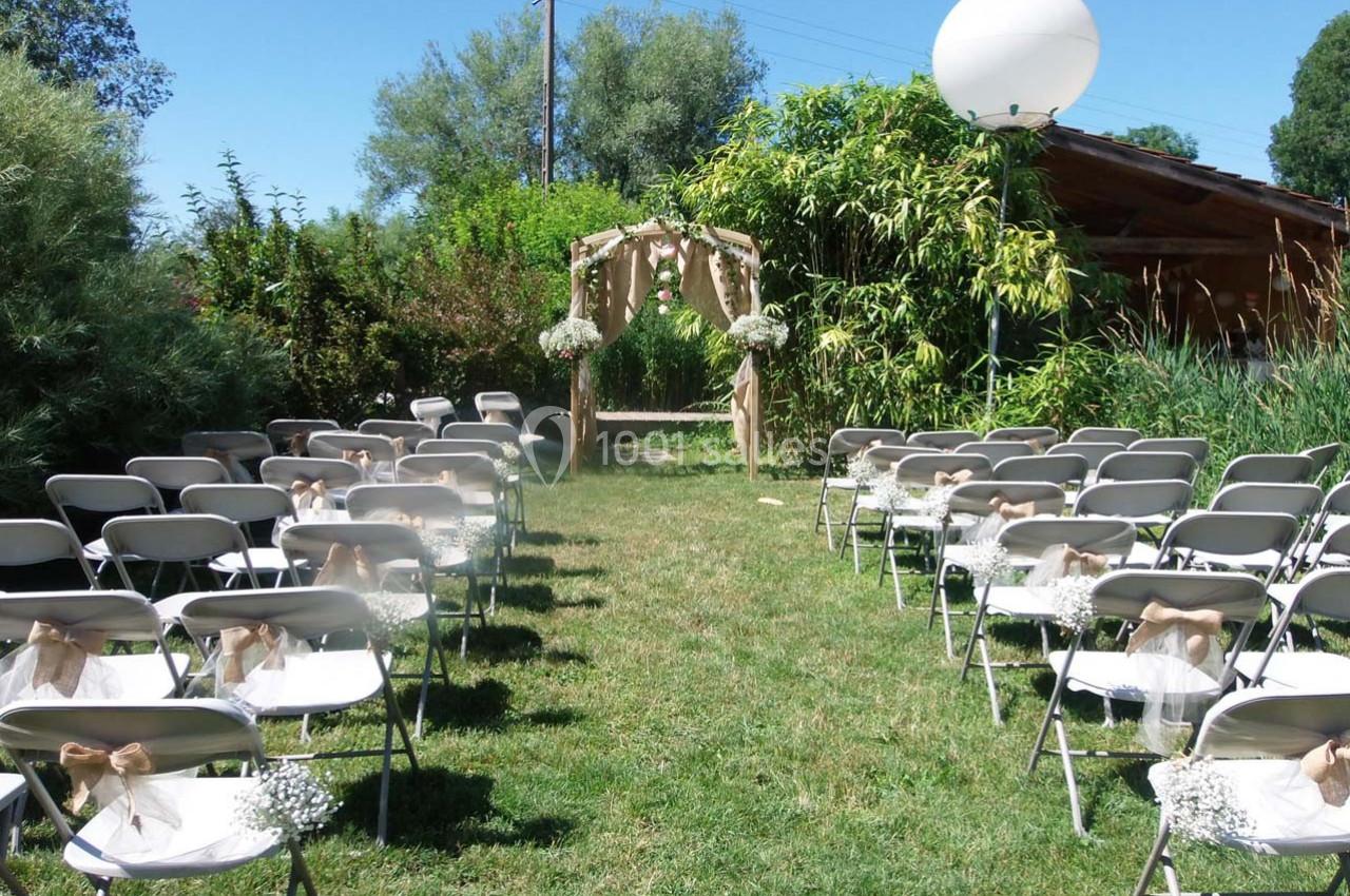 Location salle Ornacieux (Isère) - Domaine du Moulin Piongo #4 Chaises alignées sur une pelouse face à une arche décorée de fleurs, préparées pour une cérémonie en plein air.