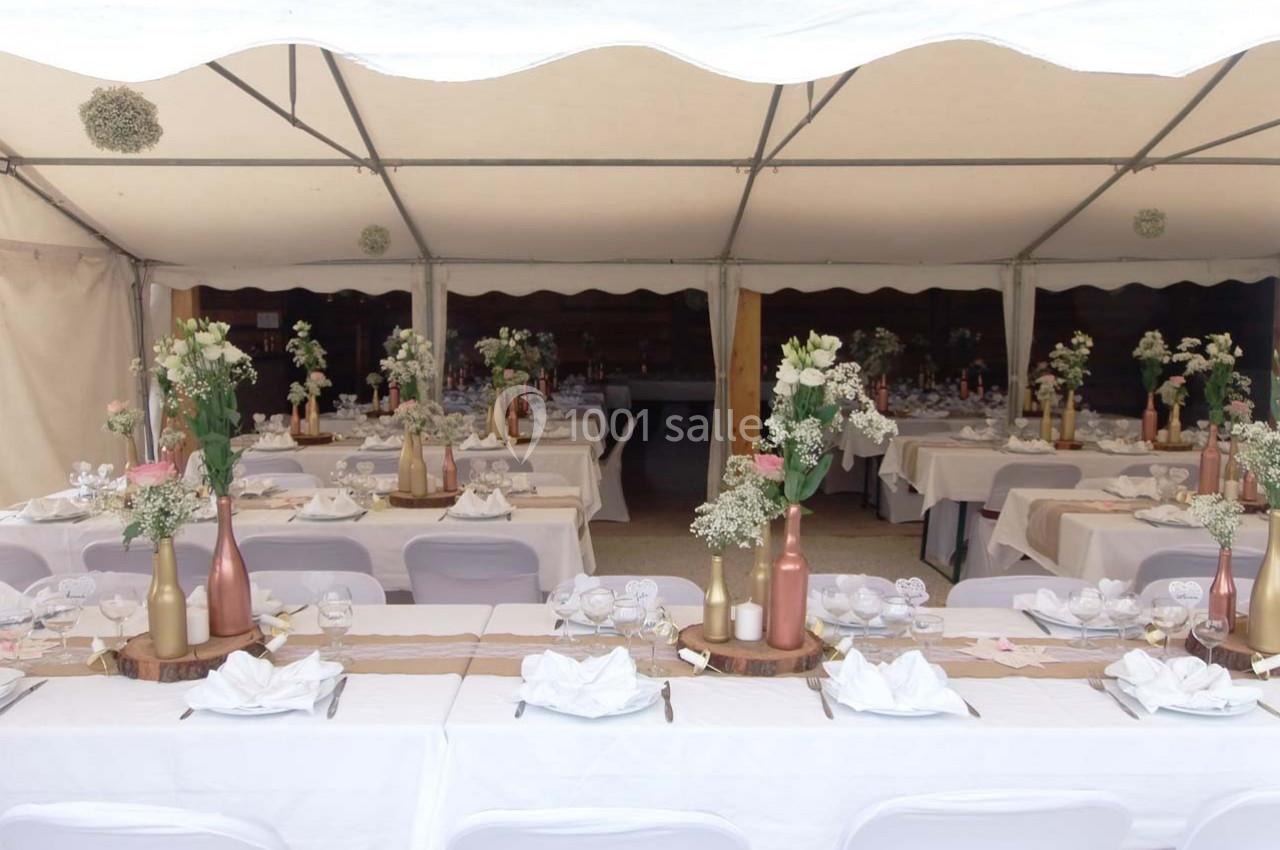 Location salle Ornacieux (Isère) - Domaine du Moulin Piongo #11 Tables décorées pour un événement sous une tente, avec nappes blanches, centres de table fleuris et vaisselle disposée.