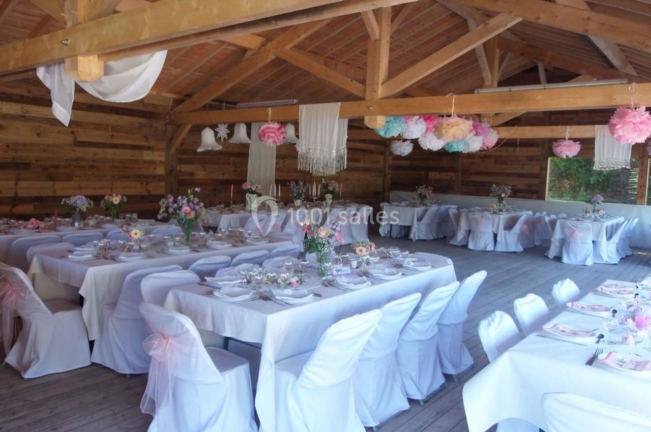 Location salle Ornacieux (Isère) - Domaine du Moulin Piongo #12 Salle de réception en bois décorée avec des tables dressées, nappes blanches et suspensions colorées.