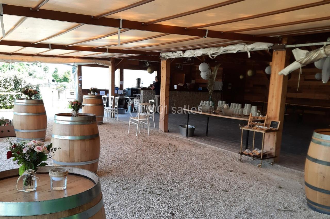 Location salle Ornacieux (Isère) - Domaine du Moulin Piongo #22 Salle de réception en plein air avec tonneaux en bois, tables décorées et espace couvert en arrière-plan.