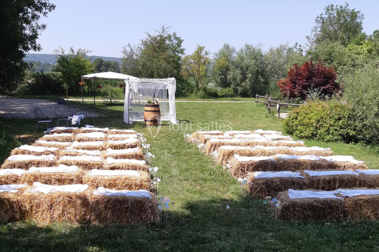Location salle Ornacieux (Isère) - Domaine du Moulin Piongo #21 Chaises en bottes de paille alignées en extérieur, face à une arche décorée pour une cérémonie champêtre.