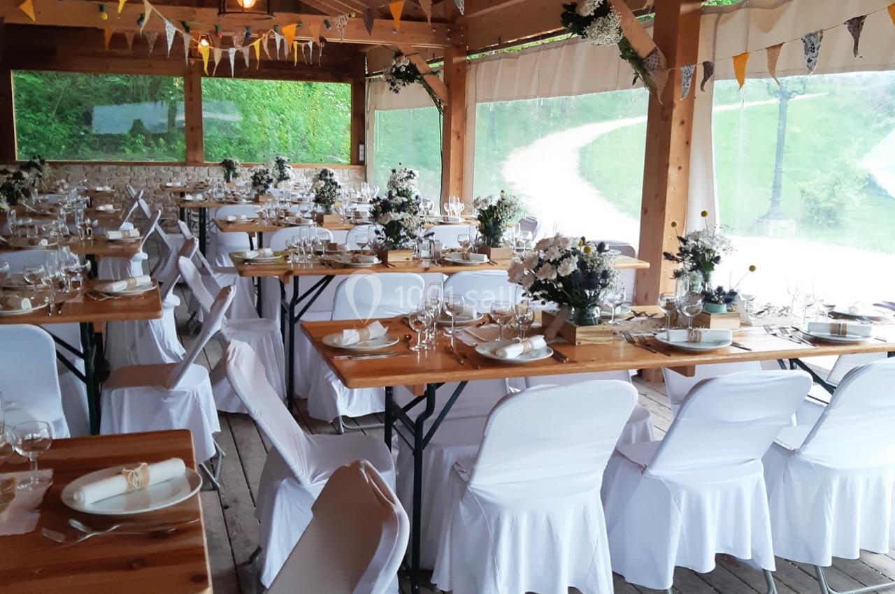 Location salle Ornacieux (Isère) - Domaine du Moulin Piongo #10 Salle de réception décorée avec des tables en bois, nappes blanches et arrangements floraux, prête pour un événement.
