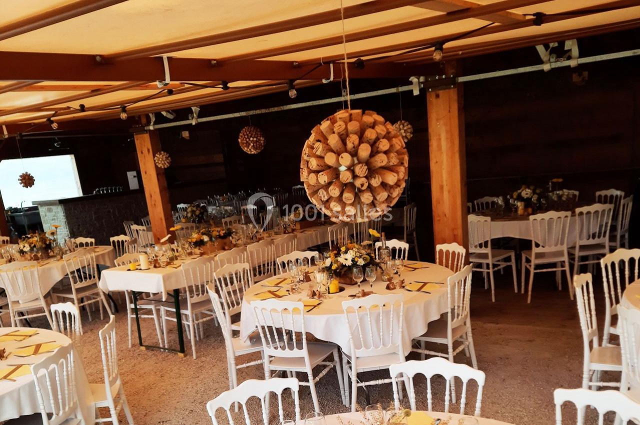 Location salle Ornacieux (Isère) - Domaine du Moulin Piongo #5 Salle décorée pour un événement, avec des tables rondes dressées, chaises blanches et suspensions en bois.