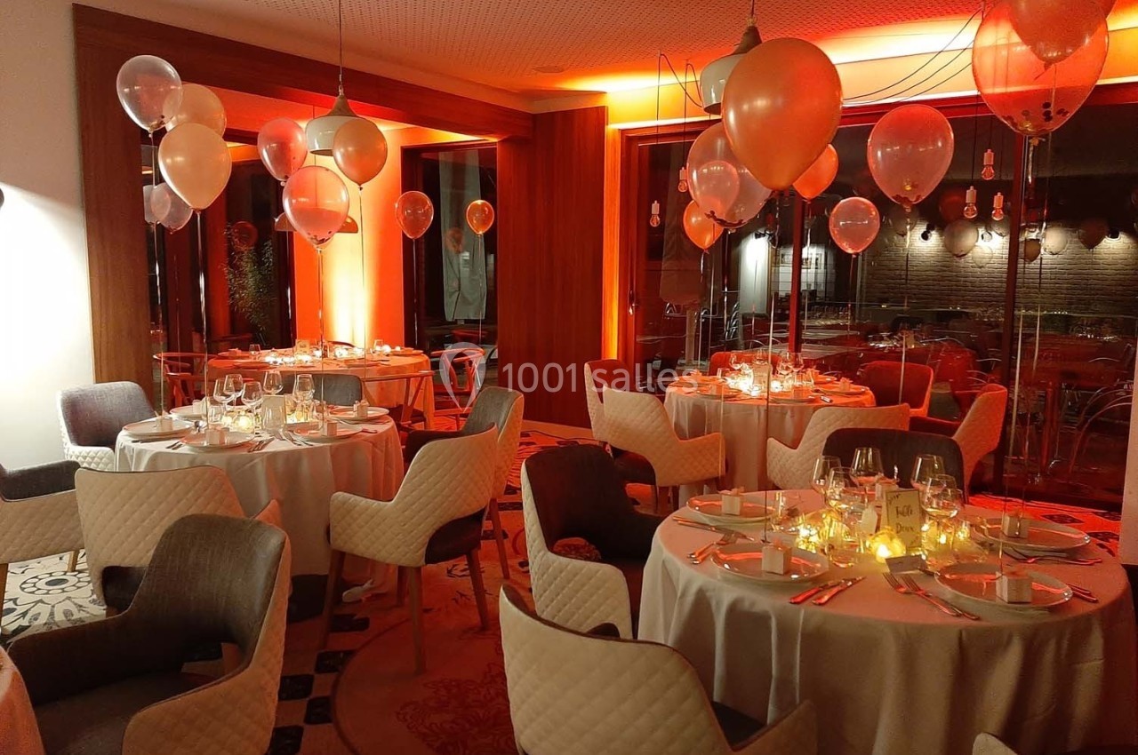 Salle de réception décorée avec des ballons et des lumières tamisées, tables dressées pour un dîner élégant.