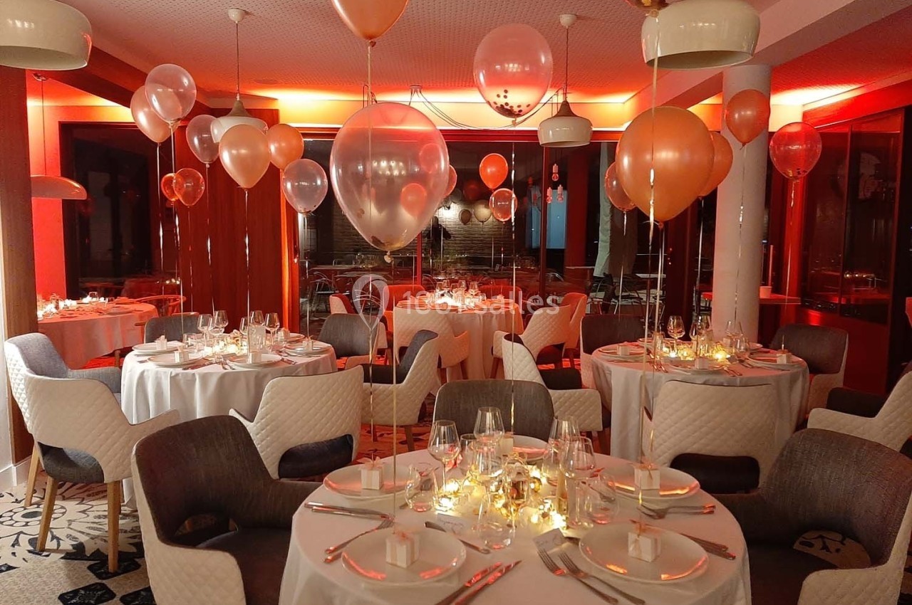 Salle de réception décorée avec des ballons et des tables dressées pour un événement festif en ambiance lumineuse…