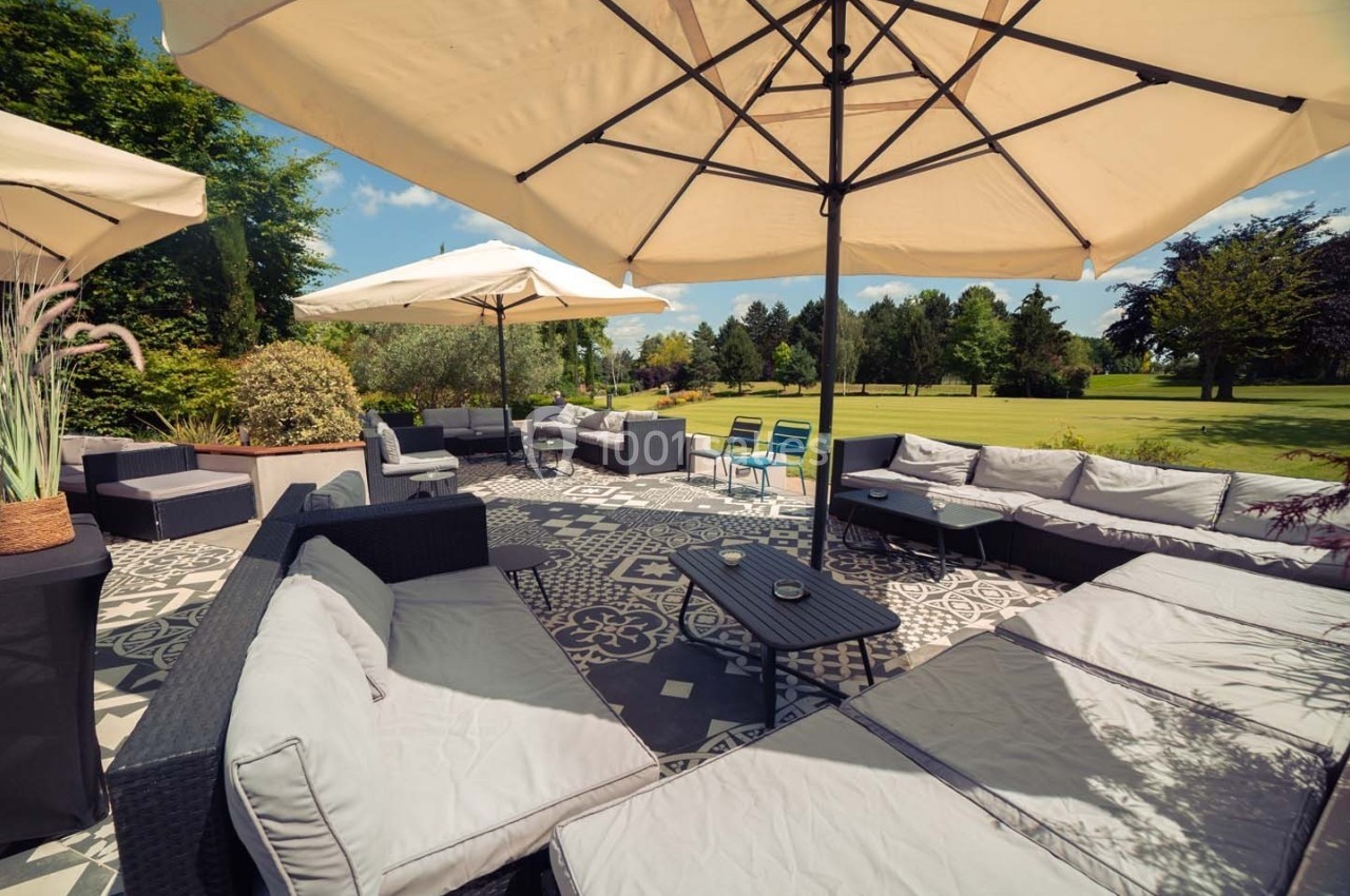 Terrasse aménagée avec canapés, tables basses et parasols, donnant sur un grand jardin verdoyant.