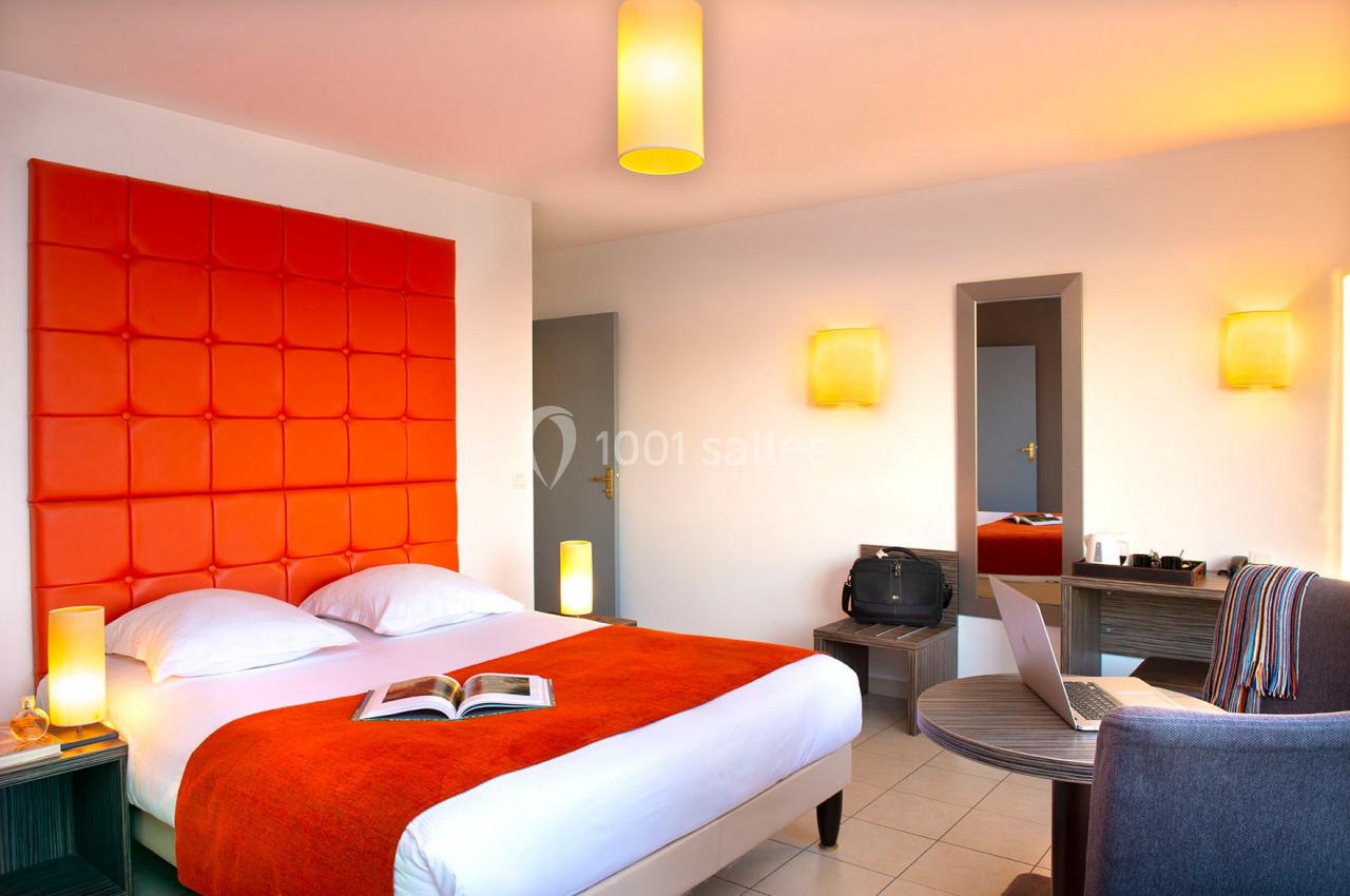 Chambre lumineuse avec lit double, tête de lit orange, bureau, chaise, et éclairage moderne.
