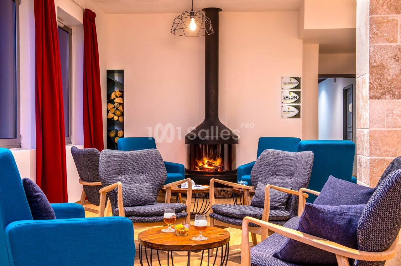 Espace salon chaleureux avec fauteuils bleus, table basse en bois et cheminée allumée dans un décor moderne.