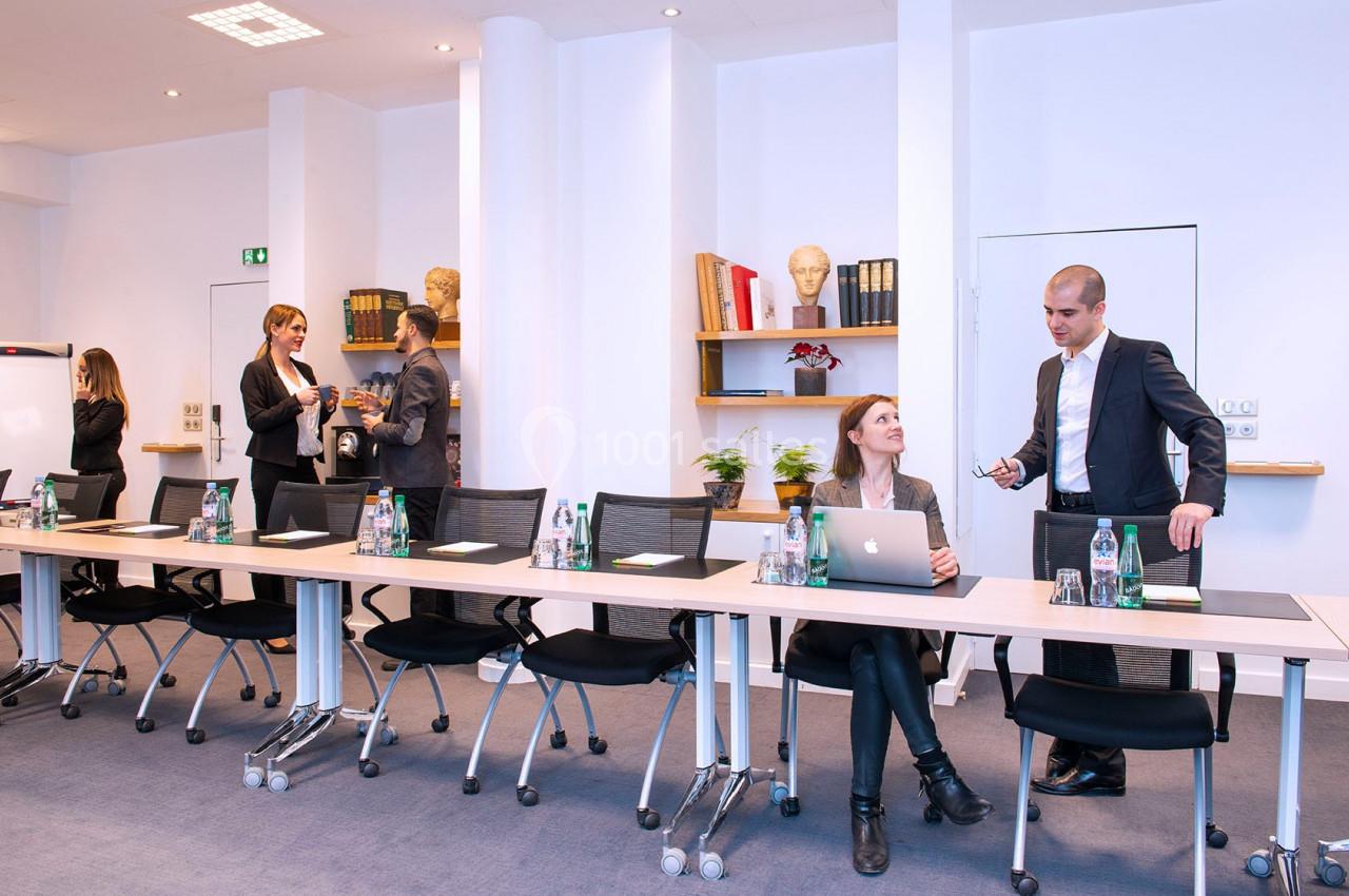 Des personnes en tenue professionnelle discutent et travaillent dans une salle de réunion équipée de tables et chaises…