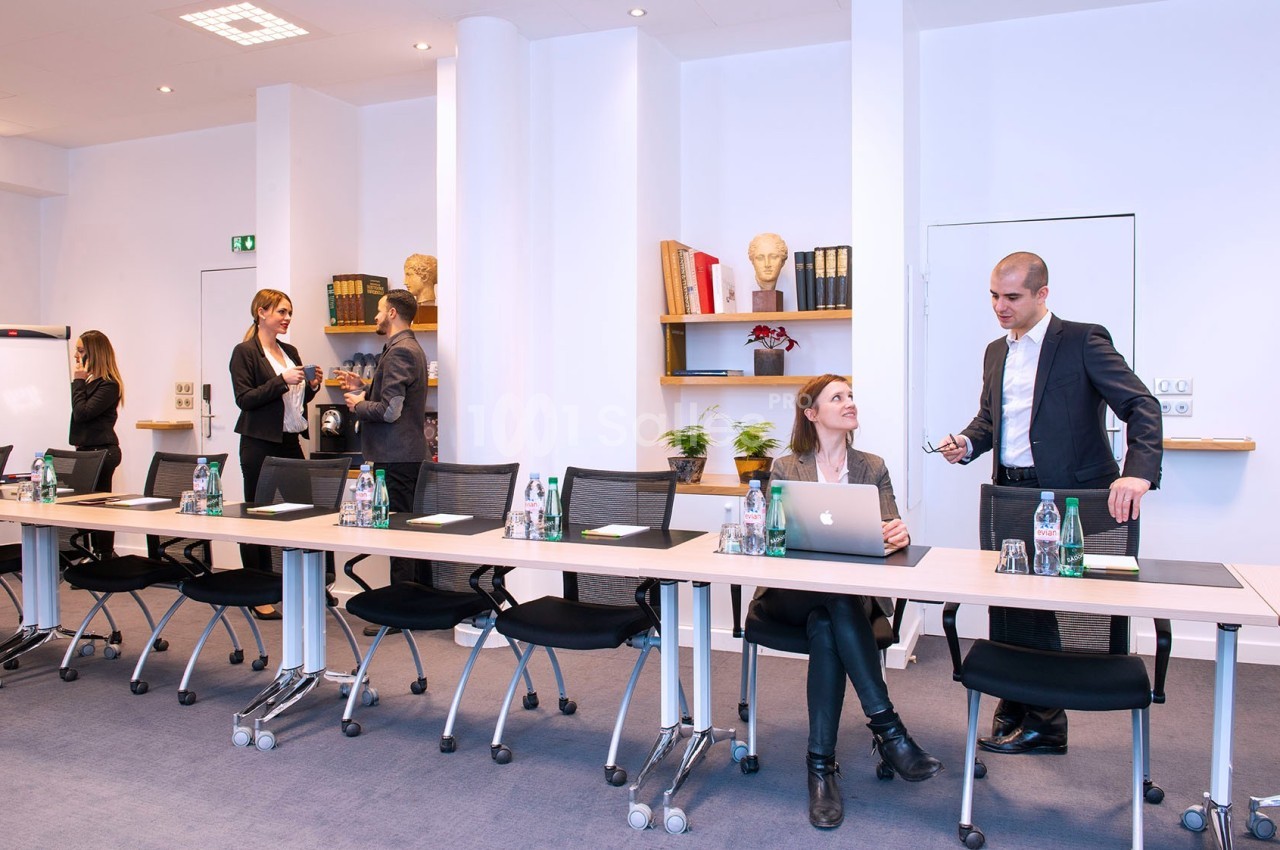 Des personnes en tenue professionnelle discutent et travaillent dans une salle de réunion équipée de tables et chaises…