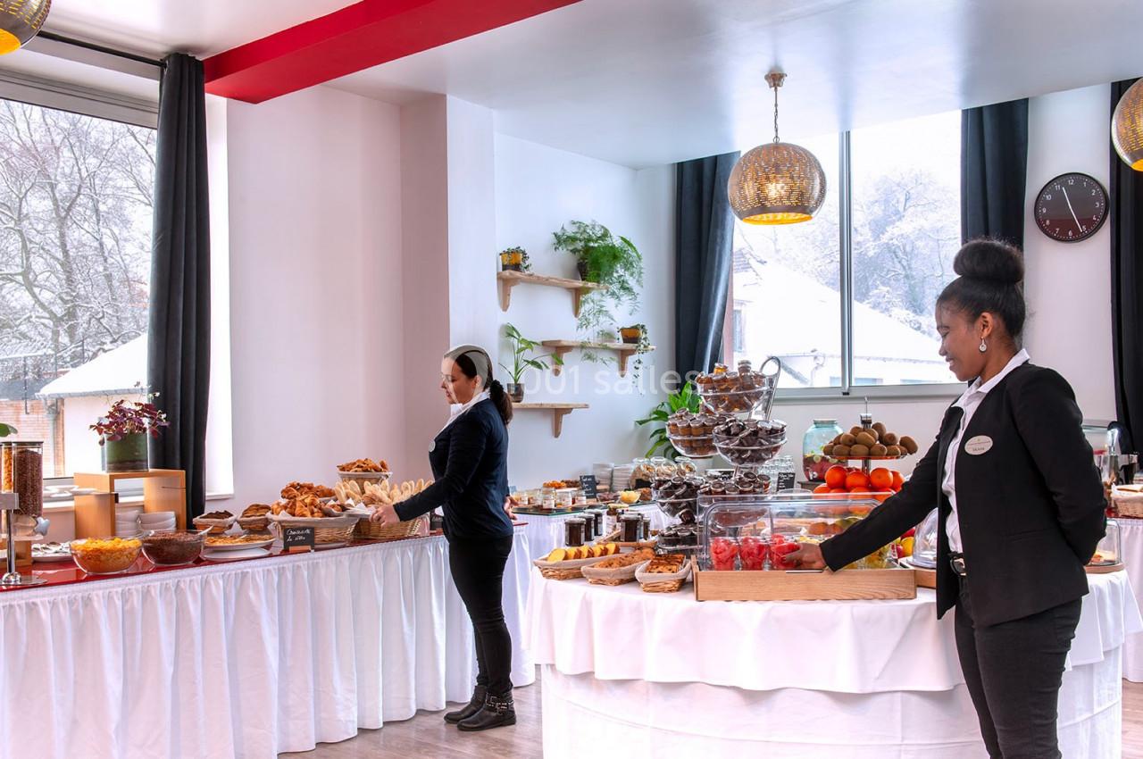 Buffet varié avec viennoiseries, fruits et desserts, dans une salle lumineuse avec vue sur un paysage enneigé.