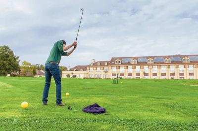 Vue d'un terrain de golf verdoyant avec des arbres et une ville en arrière-plan sous un ciel dégagé.