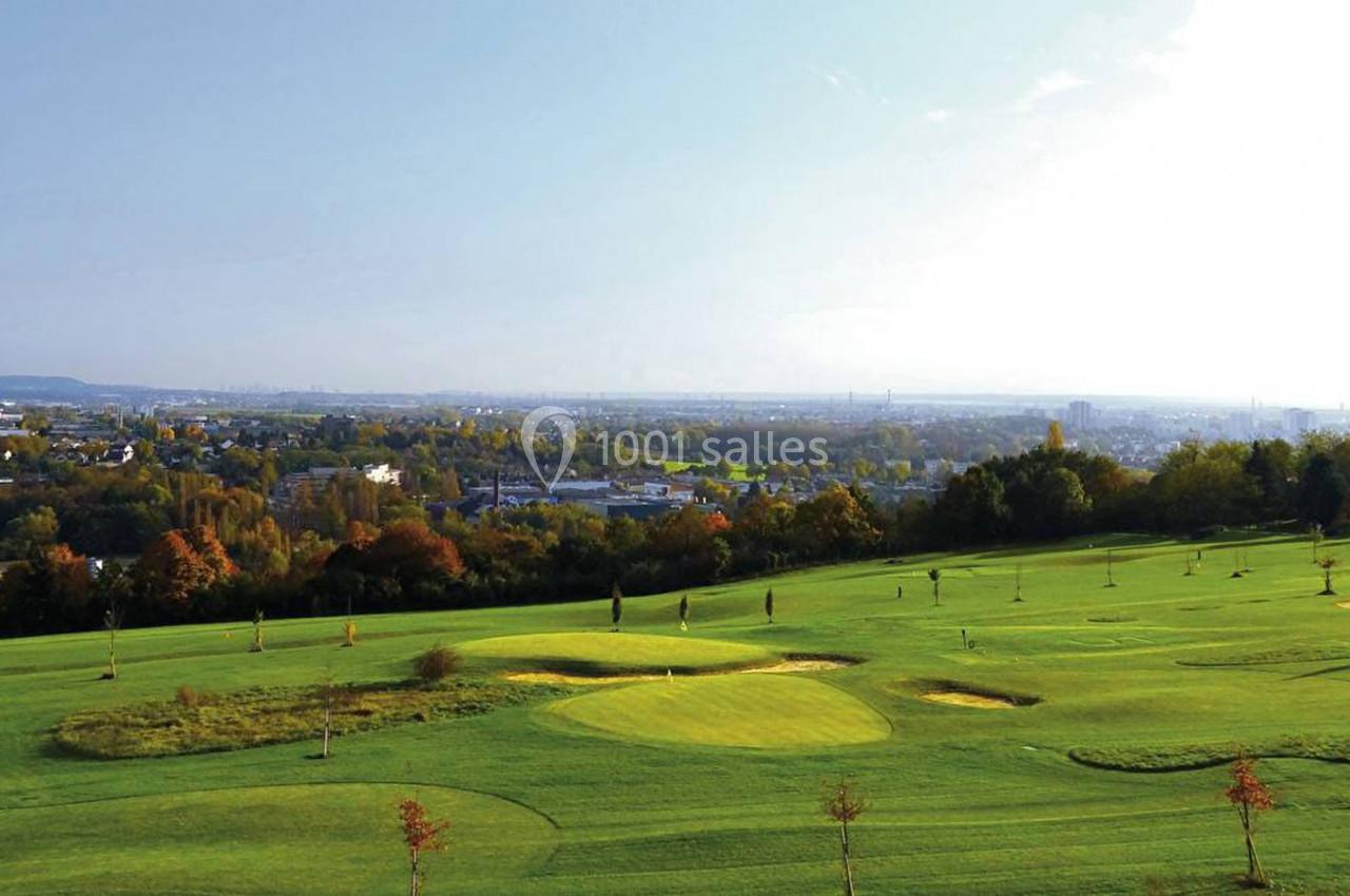 Vue d'un terrain de golf verdoyant avec des arbres et une ville en arrière-plan sous un ciel dégagé.