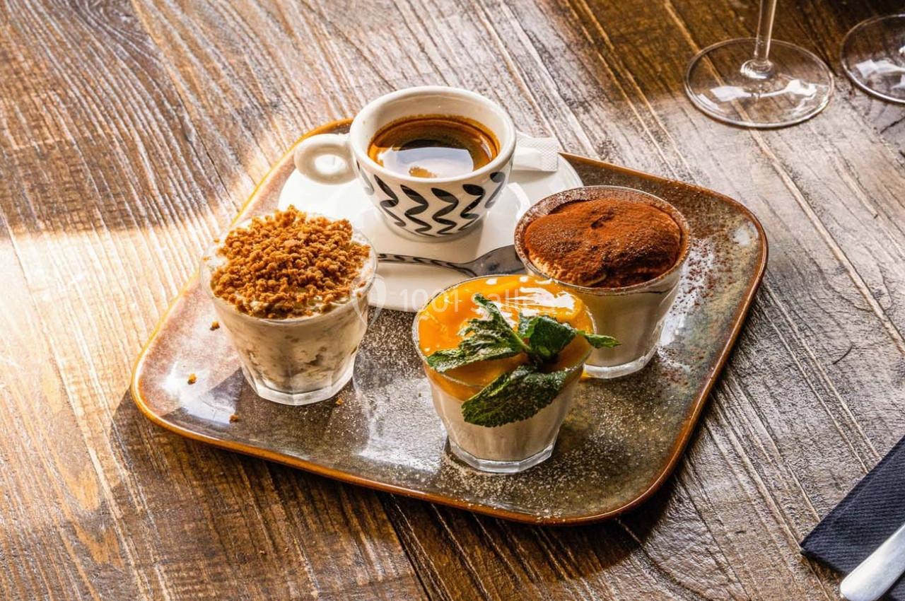 Plateau de desserts variés avec un café expresso, présenté sur une table en bois éclairée par la lumière naturelle.