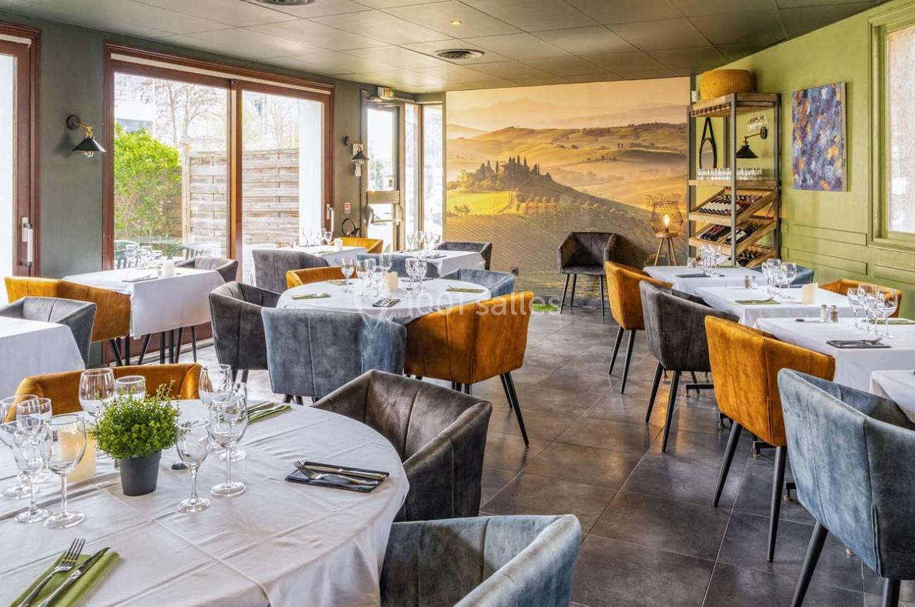 Salle de restaurant lumineuse avec tables dressées, chaises colorées et décor mural représentant un paysage de campagne.
