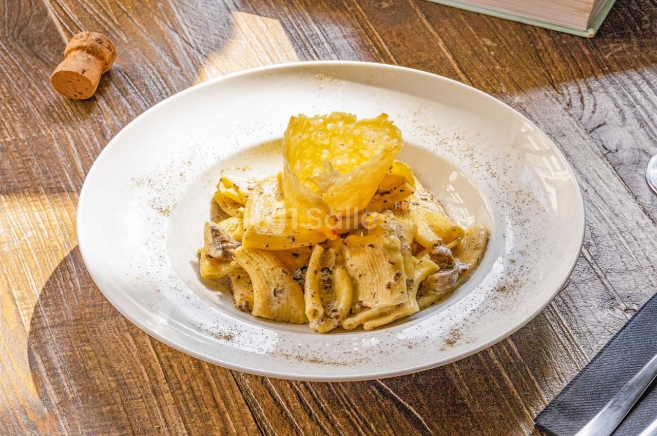 Assiette de pâtes rigatoni à la truffe avec une tuile de fromage, servie sur une table en bois.