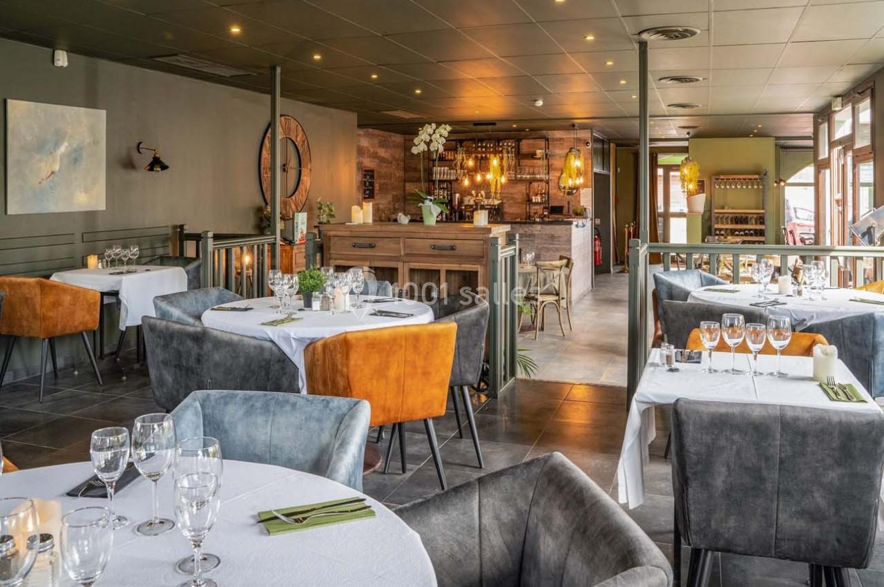 Salle de restaurant élégante avec tables dressées, chaises colorées et un bar en bois au fond.