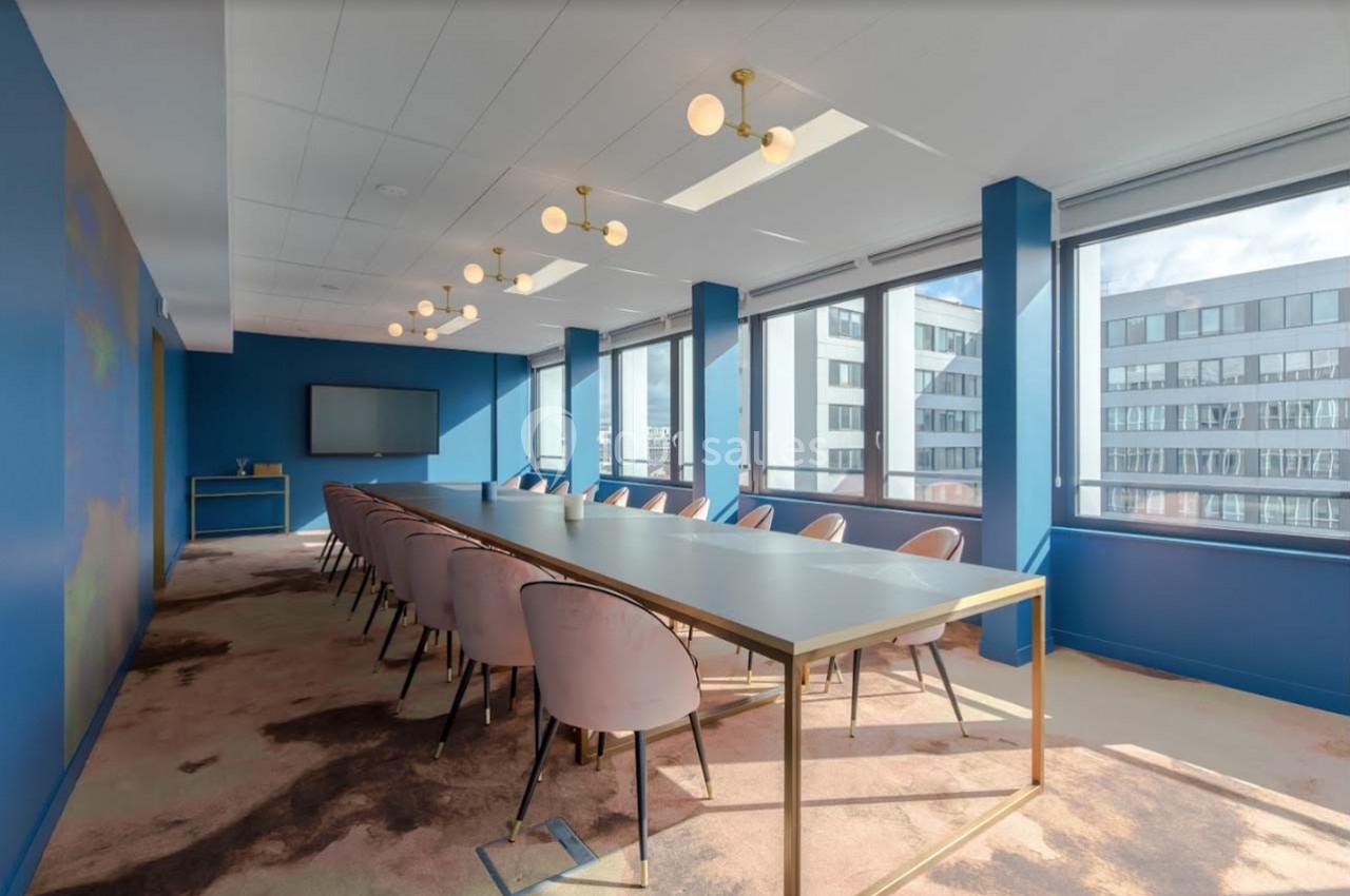 Salle de réunion lumineuse avec une grande table, des chaises roses et des fenêtres donnant sur des immeubles modernes.