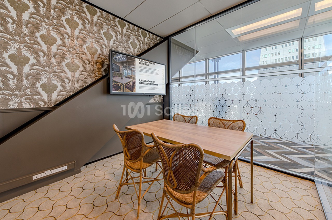 Salle de réunion avec table en bois, chaises en rotin, mur décoré de motifs végétaux et cloison vitrée partiellement opaque.