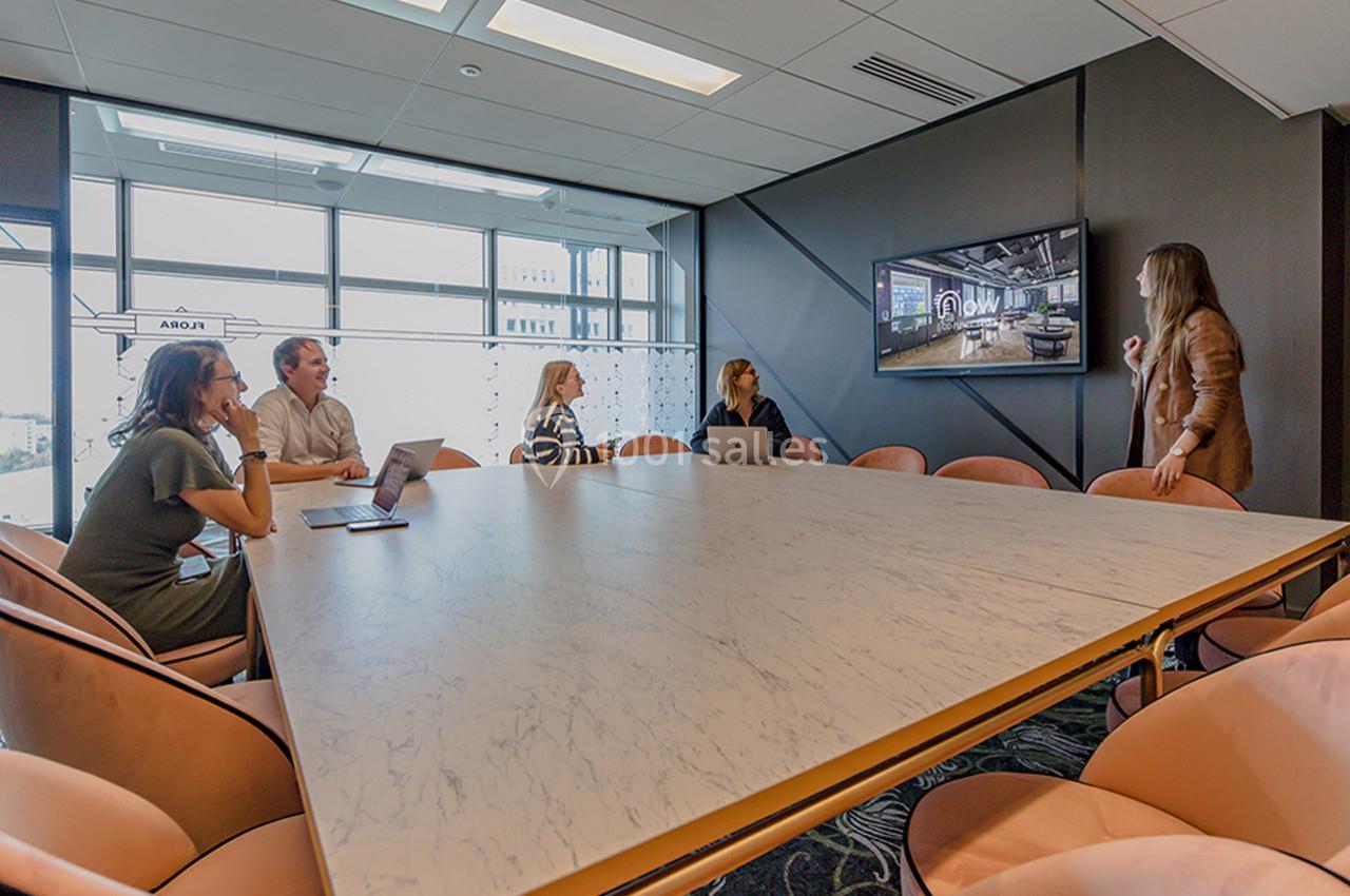 Une femme présente des informations sur un écran à un groupe de personnes assises autour d'une table de réunion.