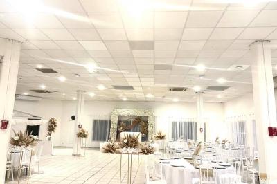 Salle de réception décorée pour un mariage, avec tables dressées, fleurs blanches et rouges, et arche florale en arrière…