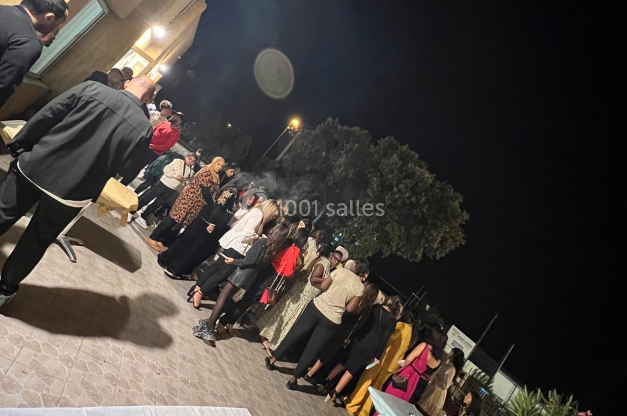 Groupe de personnes debout en extérieur la nuit, discutant et formant une file près d'un bâtiment éclairé.