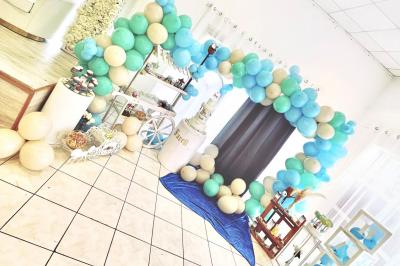 Salle de réception décorée pour un mariage, avec tables dressées, fleurs blanches et rouges, et arche florale en arrière…