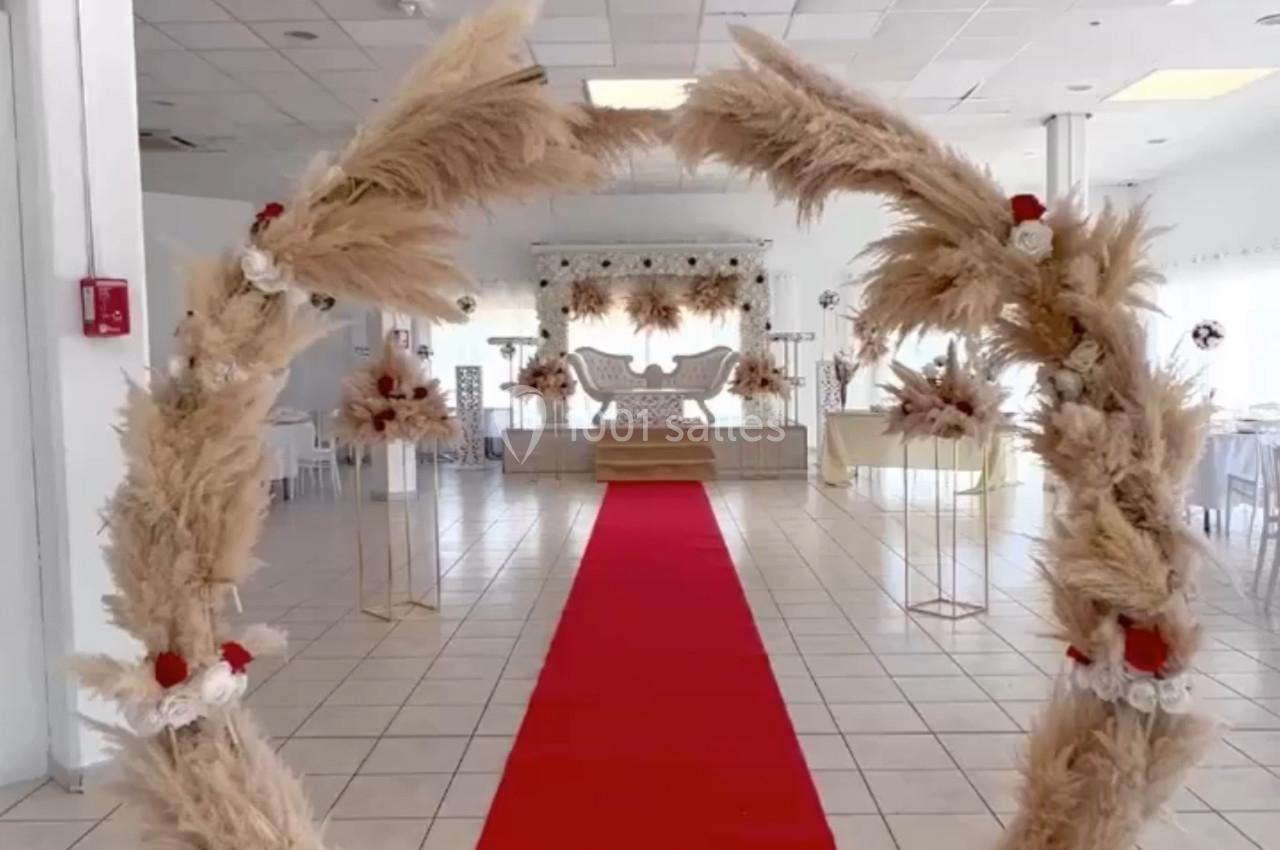 Arche décorative en pampas avec tapis rouge menant à une salle de réception lumineuse et aménagée.