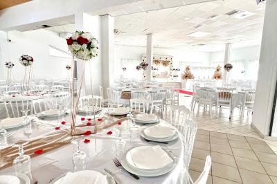 Salle de réception décorée pour un mariage, avec tables dressées, fleurs blanches et rouges, et arche florale en arrière…