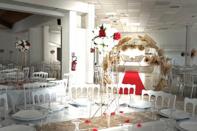 Salle de réception décorée pour un mariage, avec tables dressées, fleurs blanches et rouges, et arche florale en arrière…