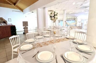 Salle de réception décorée pour un mariage, avec tables dressées, fleurs blanches et rouges, et arche florale en arrière…