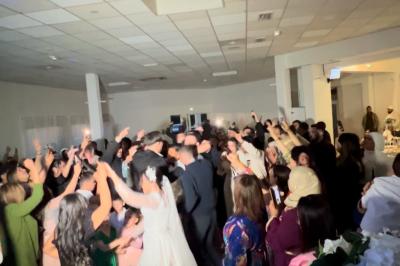 Salle de réception décorée pour un mariage, avec tables dressées, fleurs blanches et rouges, et arche florale en arrière…