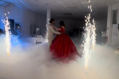 Salle de réception décorée pour un mariage, avec tables dressées, fleurs blanches et rouges, et arche florale en arrière…