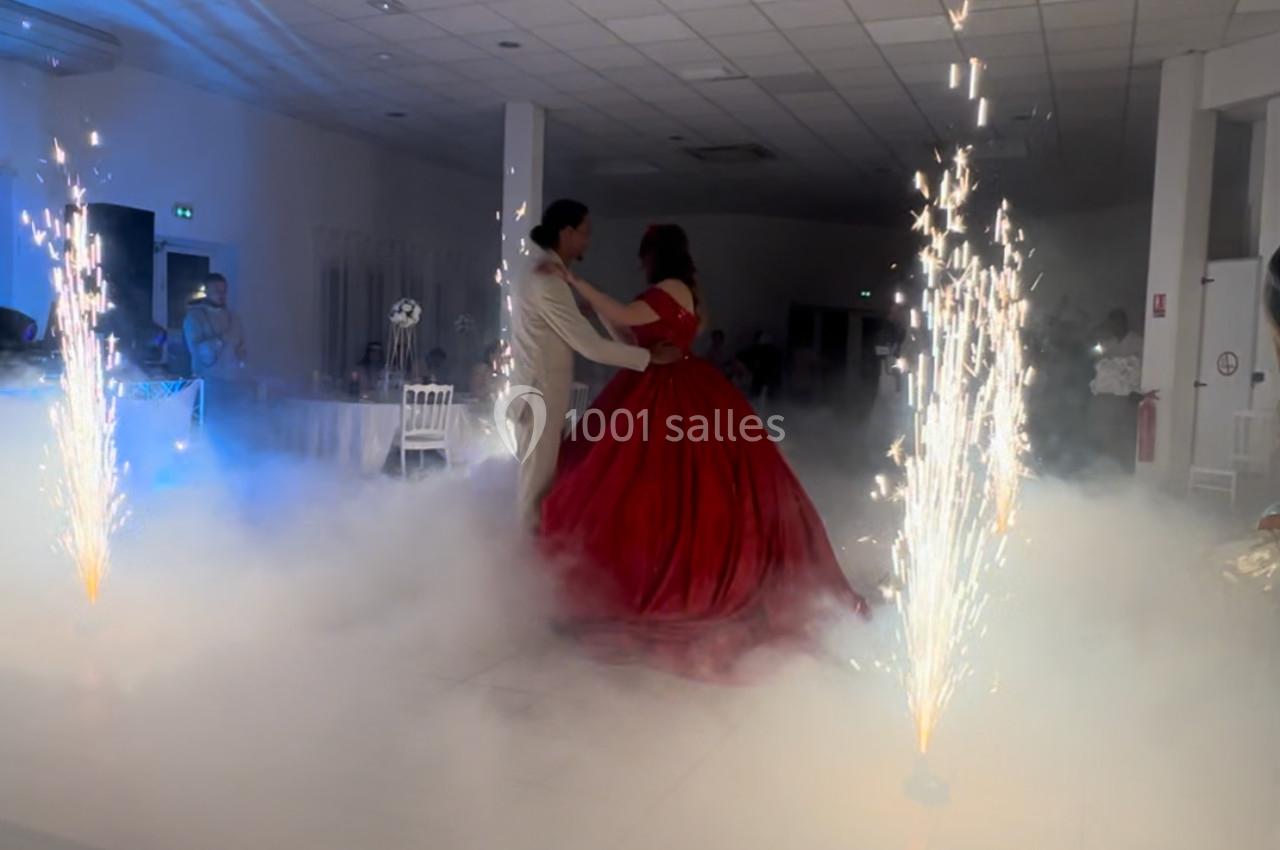 Un couple danse au centre d'une salle illuminée, entouré de fumée et de fontaines d'étincelles.