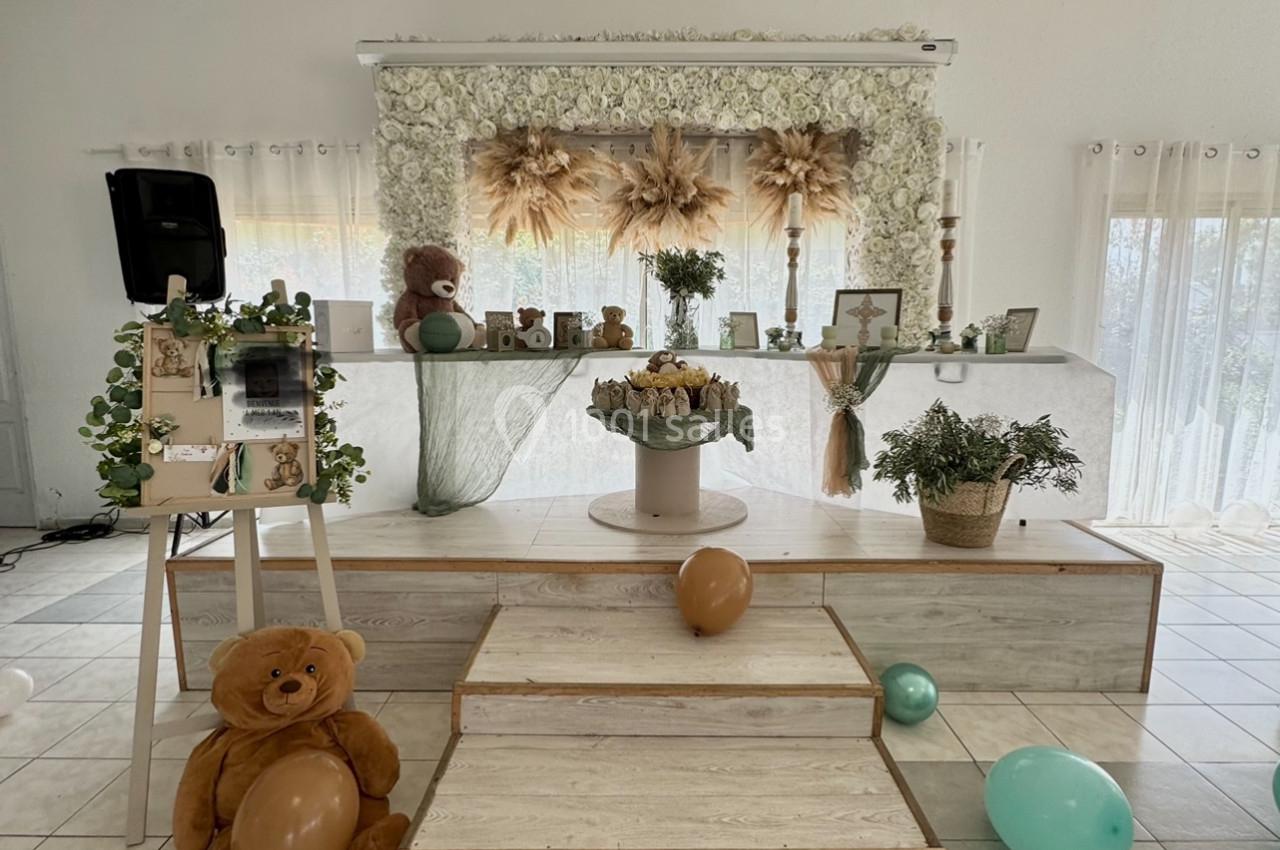 Décoration de salle avec ballons, ours en peluche et fleurs séchées sur une estrade, ambiance douce et lumineuse.