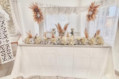 Salle de réception décorée pour un mariage, avec tables dressées, fleurs blanches et rouges, et arche florale en arrière…