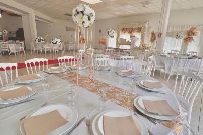 Salle de réception décorée pour un mariage, avec tables dressées, fleurs blanches et rouges, et arche florale en arrière…